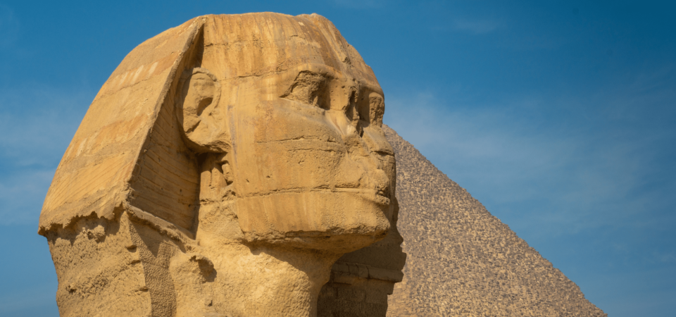 The Sphinx of Giza with the Great Pyramid in the background under a clear blue sky.