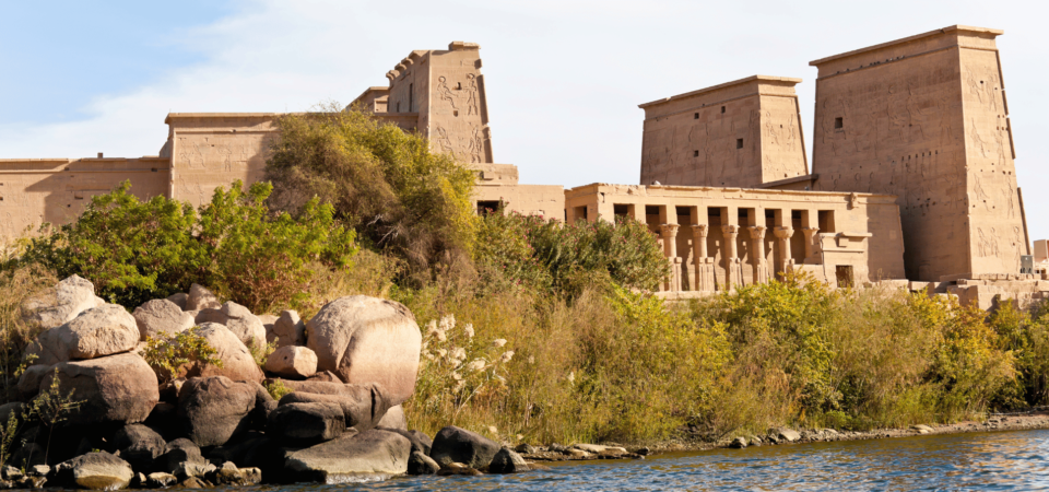 View of the Philae Temple surrounded by lush vegetation, captured from the Nile River.