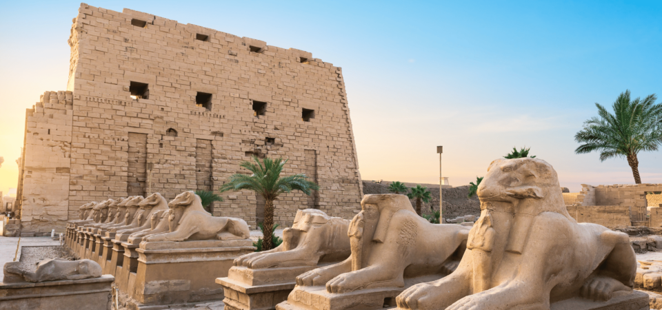 The Avenue of Sphinxes leading to the Karnak Temple's main entrance at sunset.