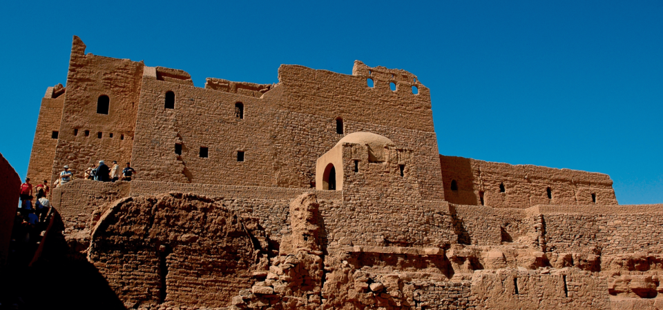 A panoramic view of the ancient Monastery of St. Simeon in Aswan, Egypt, showcasing its impressive mudbrick and stone architecture under a clear blue sky.