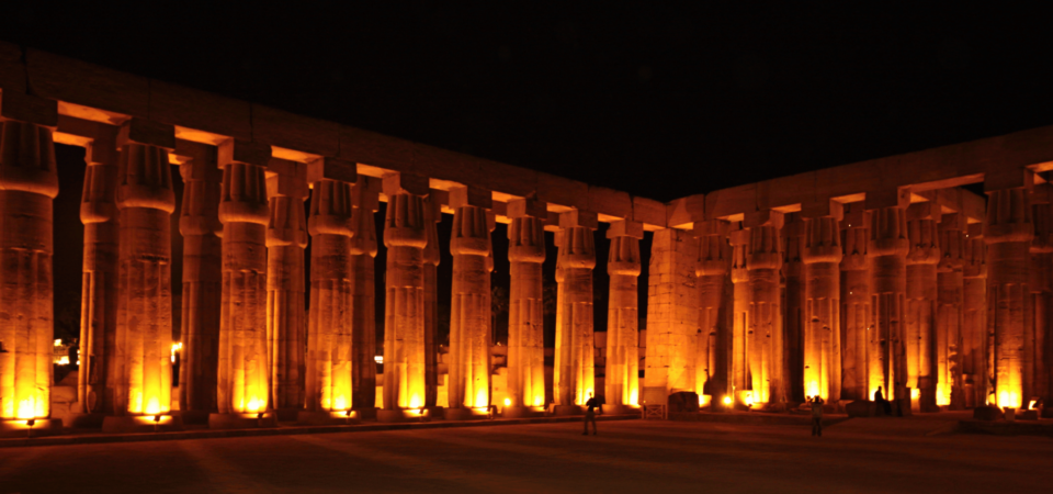 Luxor Temple's colonnade lit with golden lights at night.